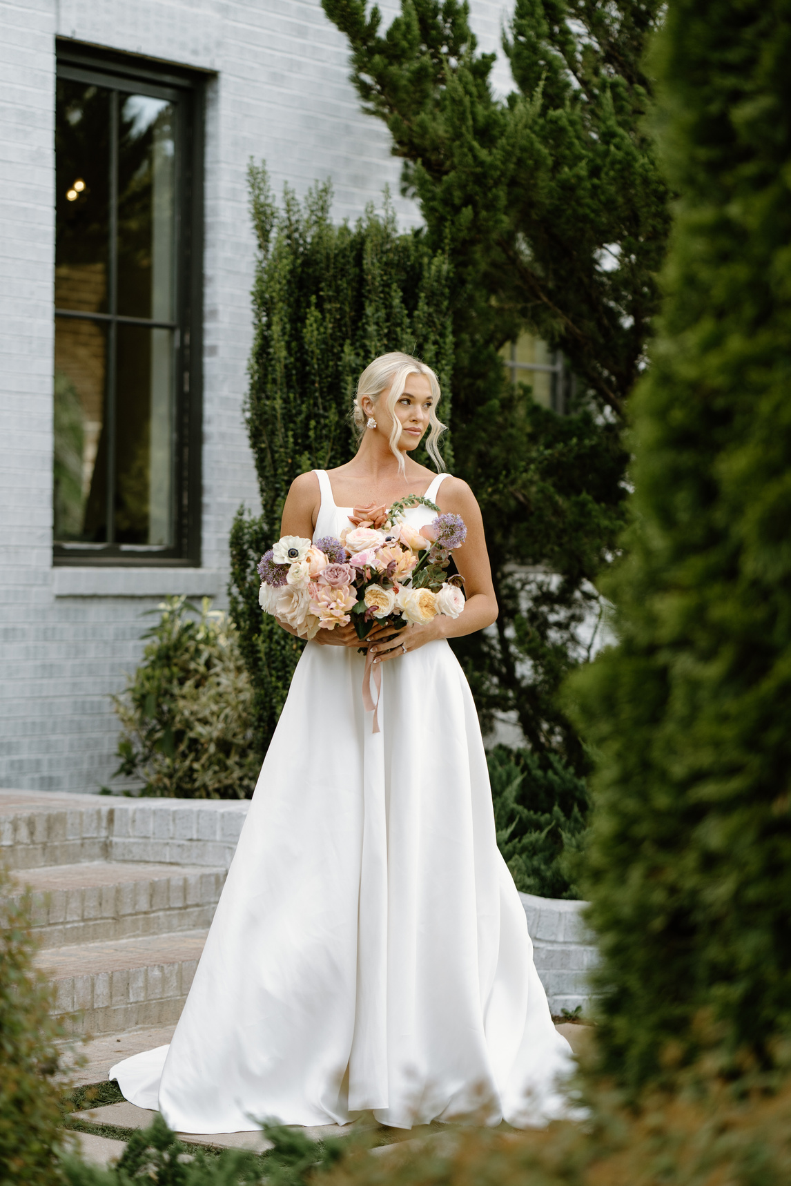 A person standing in front of a white brick building holding a bouquet