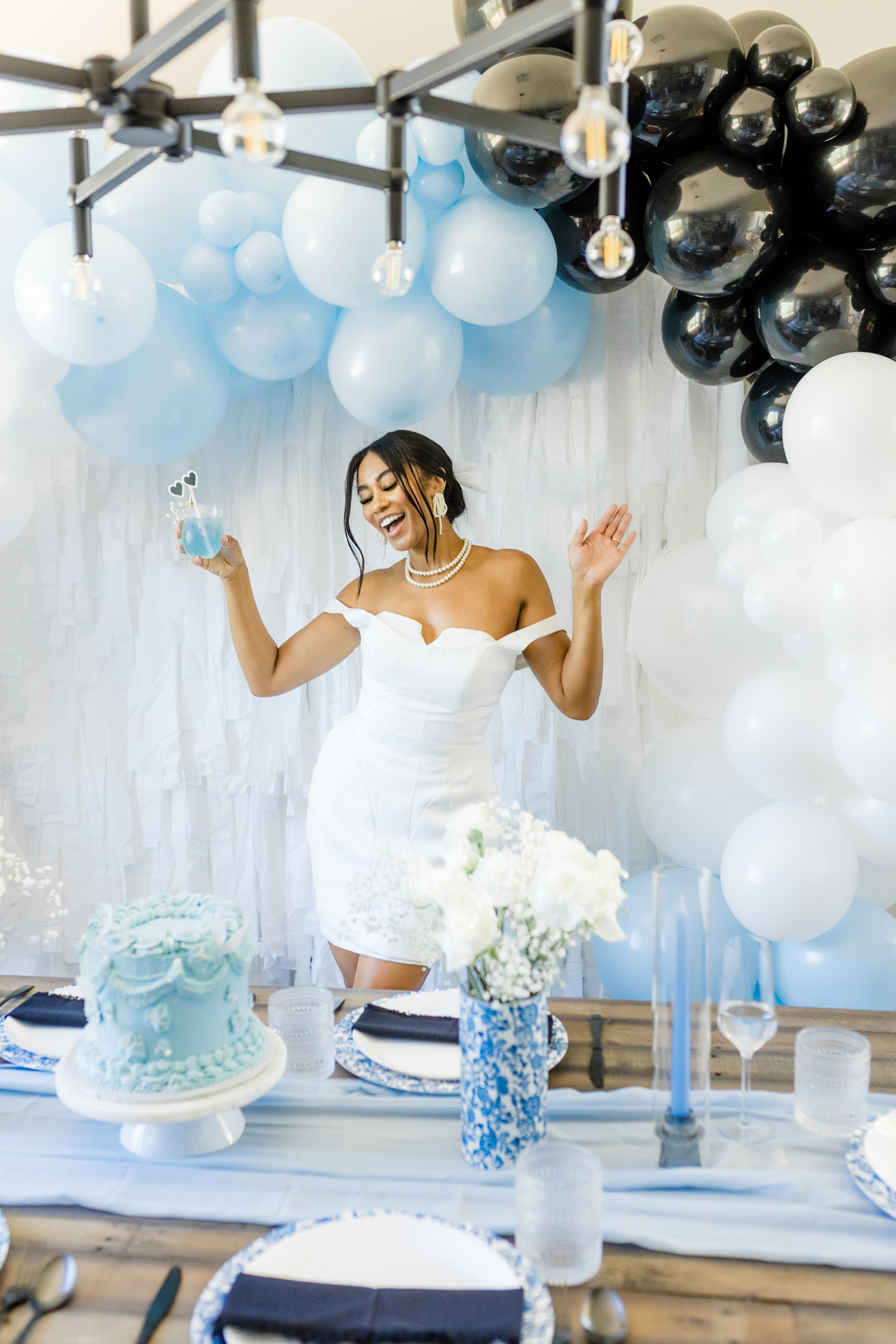 a person in a white dress standing in front of blue and white balloons