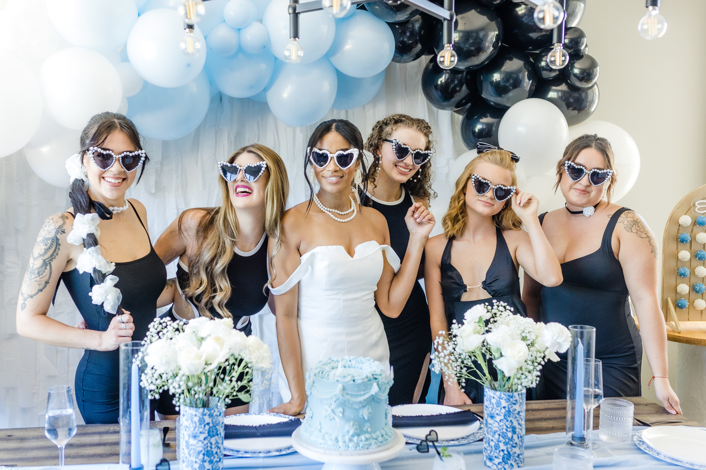 A bride and bridesmaids pose for a photo in front of a blue and white wedding cake